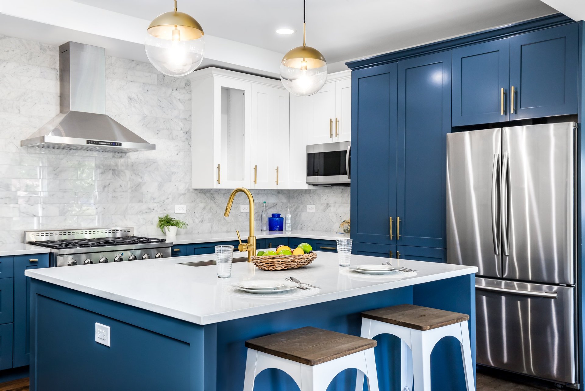A luxurious white and blue kitchen with gold hardware, stainless steel appliances, and white marbled granite counter tops