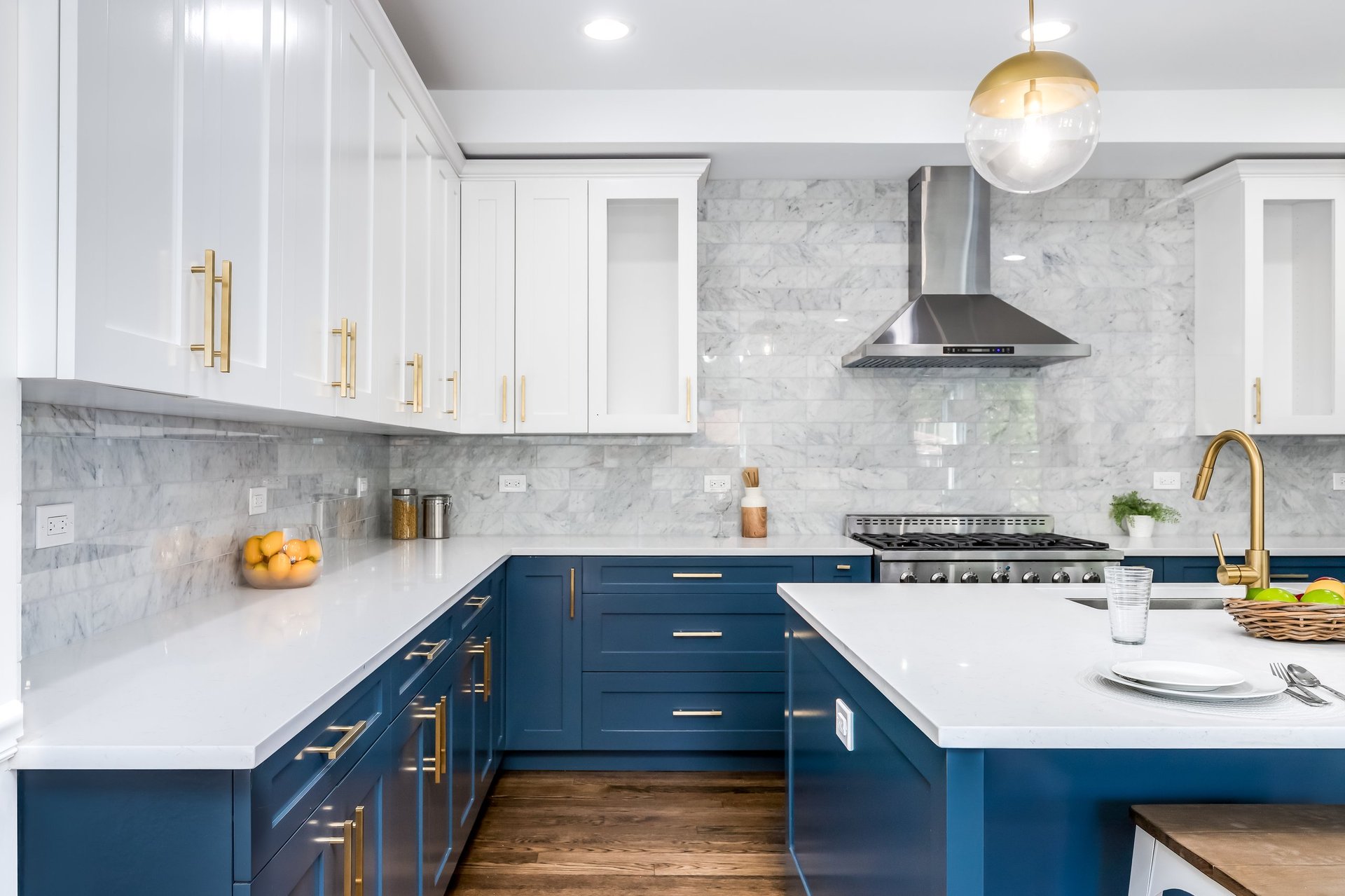 A luxurious white and blue kitchen with gold hardware, stainless steel appliances, marble subway tile backsplash, and white marble granite countertops