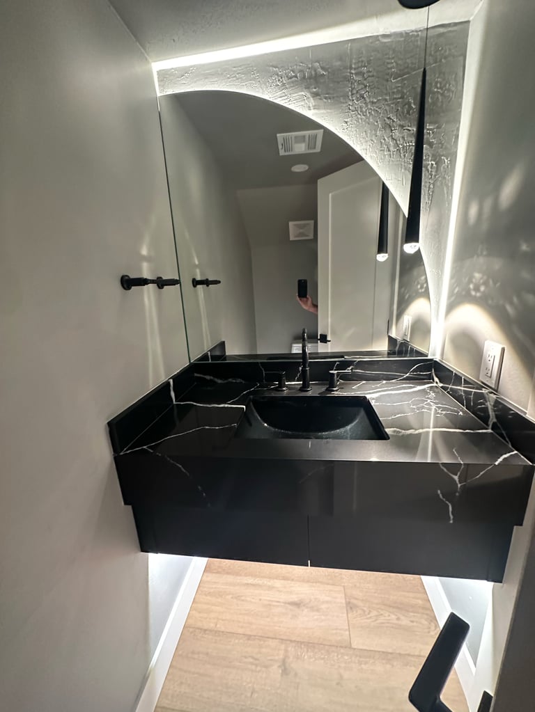 Modern bathroom vanity with black marble countertop, circular sink, and LED-lit mirror in contemporary white space
