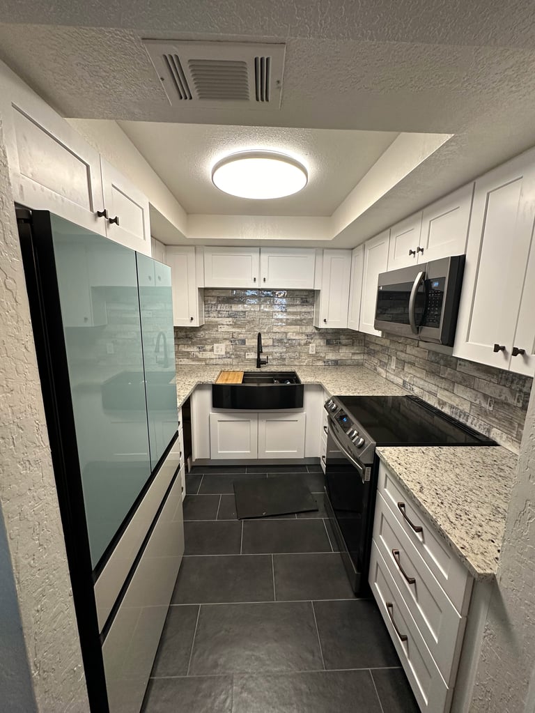 Modern galley kitchen with white cabinets, gray tile backsplash, black appliances, and granite countertops