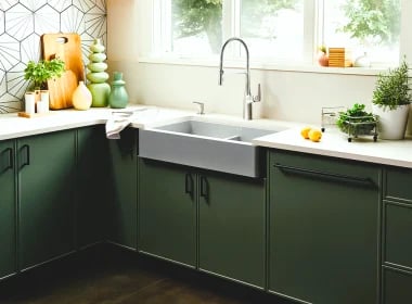 Modern kitchen with green cabinets, white countertop, farmhouse sink, and fresh produce and plants on counter