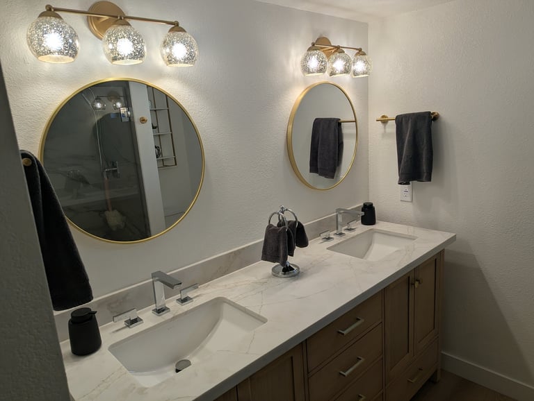 Modern bathroom with double vanity sink, two round mirrors with brass frames, and decorative light fixtures above