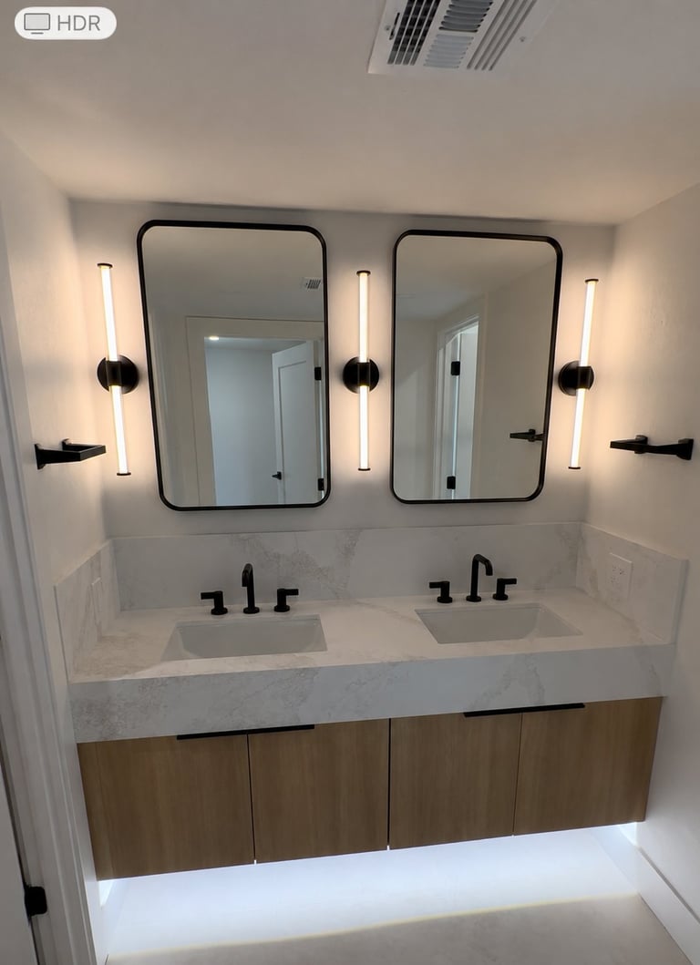 Modern bathroom with dual sinks, two framed mirrors with black frames, and vertical sconce lighting on white walls above wood vanity cabinets