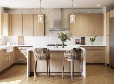 Modern kitchen with light wood cabinets, white island, two bar stools, pendant lights, and stainless steel appliances.