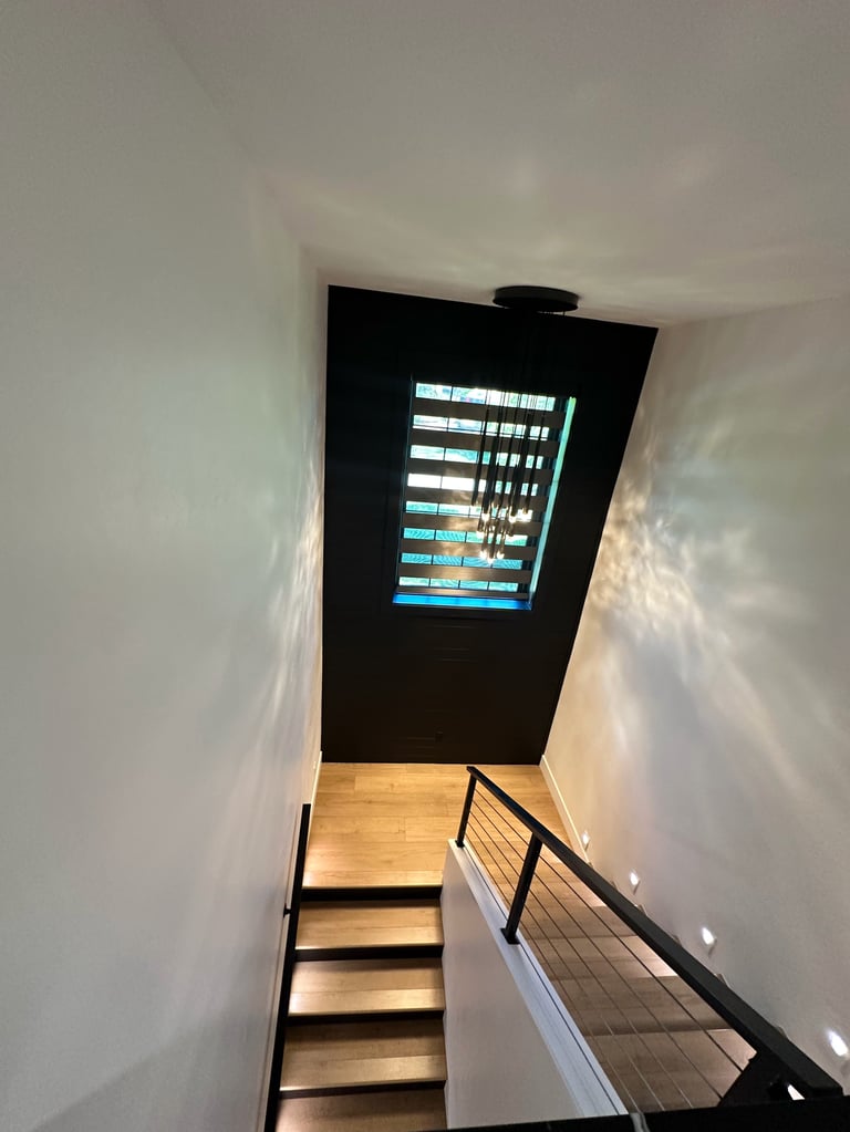 Staircase with wooden steps and metal railing leading upward to a screen displaying data at the top against white walls