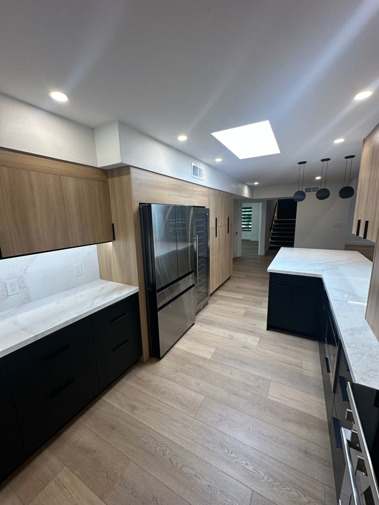 Modern kitchen with wood cabinets, stainless steel refrigerator, white countertops, skylight, and hardwood flooring