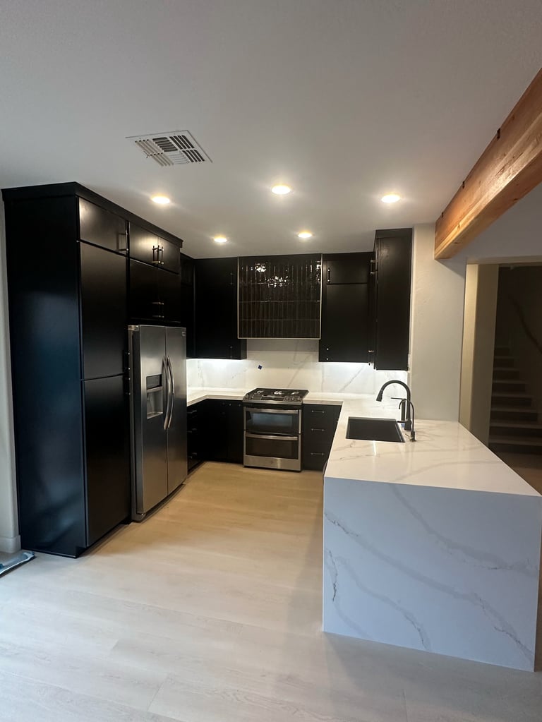 Modern kitchen with black cabinetry, stainless steel appliances, white marble island, and recessed lighting