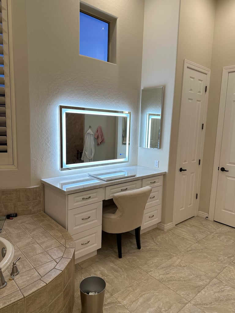 Modern bathroom vanity with lighted mirror, white cabinetry, and makeup desk chair in contemporary home
