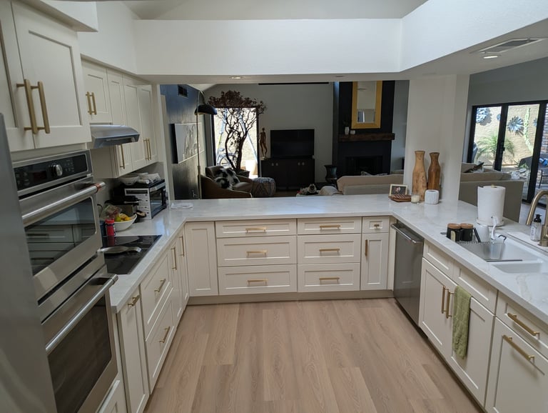 Modern kitchen with white cabinetry, stainless steel appliances, white countertops, and light wood flooring in an open floor plan layout.