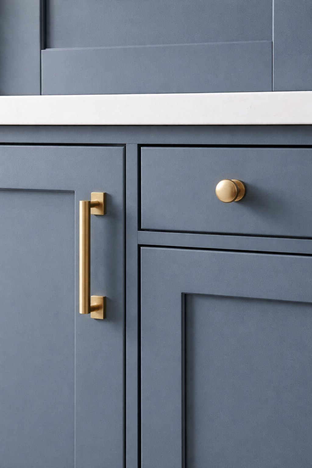 Close-up of blue-gray kitchen cabinets with brass pull handle and round knob hardware.