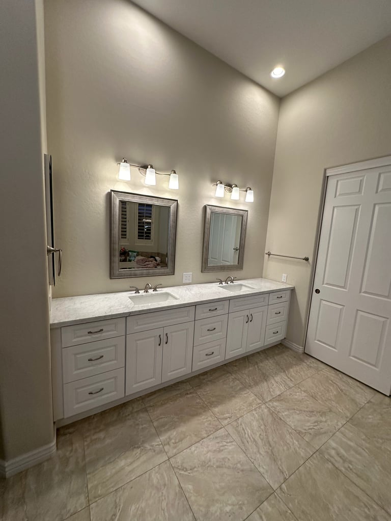 Modern bathroom with white double vanity, two mirrors, sconces, marble countertop, and tile flooring with white doors