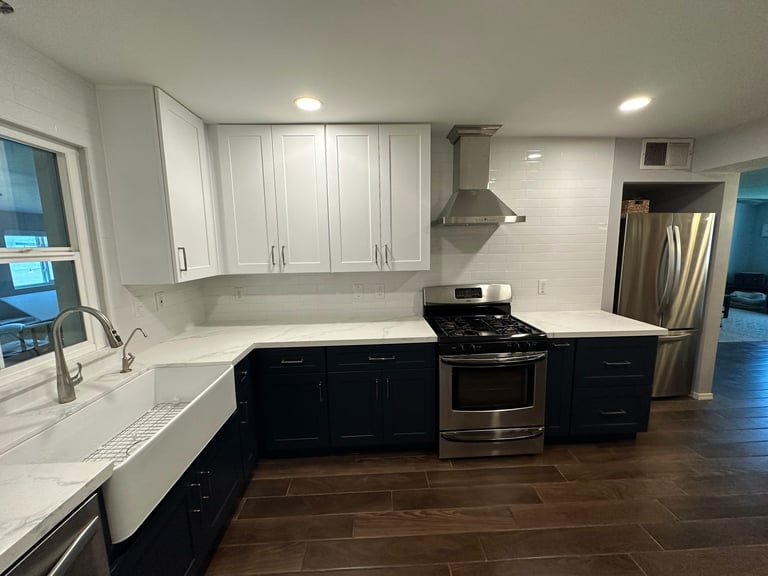 Modern kitchen with white upper cabinets, black lower cabinets, stainless steel appliances, white countertops, and dark hardwood flooring.