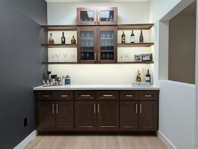 Modern home bar with dark wood cabinetry, floating shelves displaying wine bottles and glassware, and white countertop