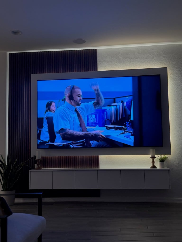 Large wall-mounted TV displaying people in an office setting with blue lighting, mounted above a dark cabinet in a modern living room